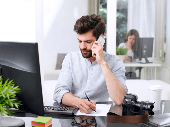 administrative assistant diploma graduate on the phone sitting at a desk in front of a laptop