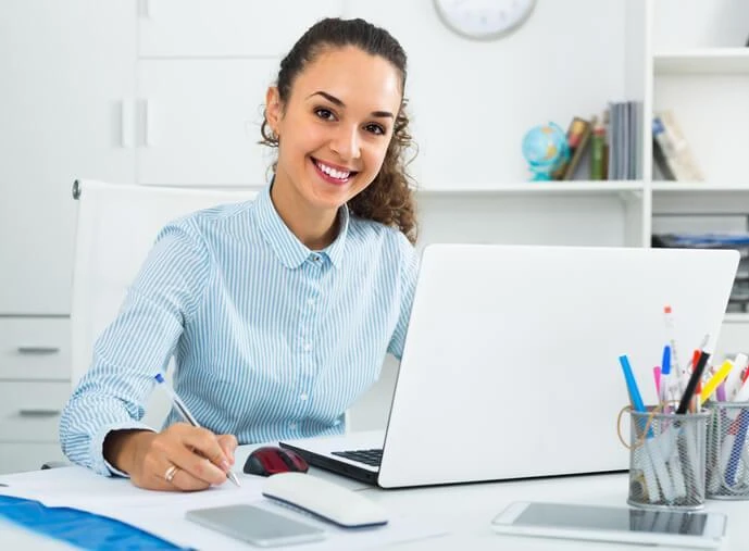 A smiling female administrative assistant in an office after completing her administrative assistant diploma program.