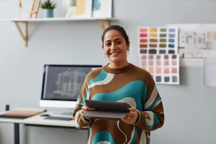 A smiling female graphic designer working on a digital tablet after completing her graphic design training