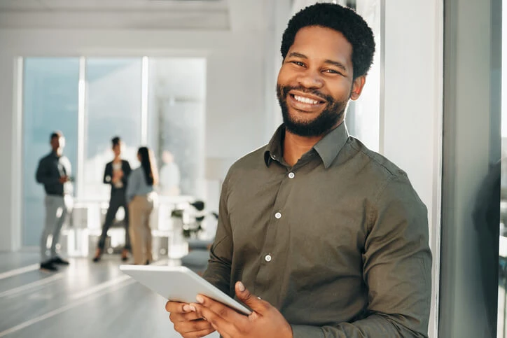 A male business administration training graduate holding a tablet in an office.