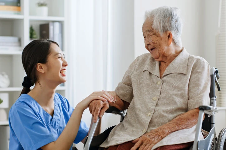 A cheerful female home support worker interacting with a smiling elderly female patient.