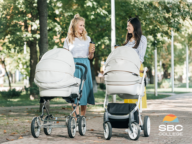 Two moms with strollers talking in a park, sharing ideas about flexible jobs for moms returning to work.