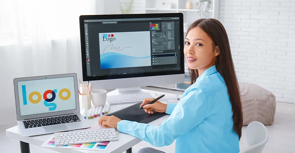A graphic designer working at her desk with two monitors, applying design principles as she studies a sheet of paper.