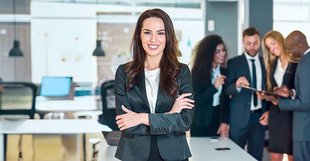 An office manager standing in a boardroom with her team discussing in the background.