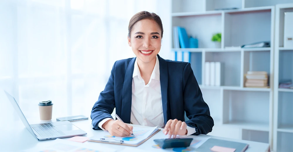 Female accountant reviewing financial documents and using a calculator in an office setting.
