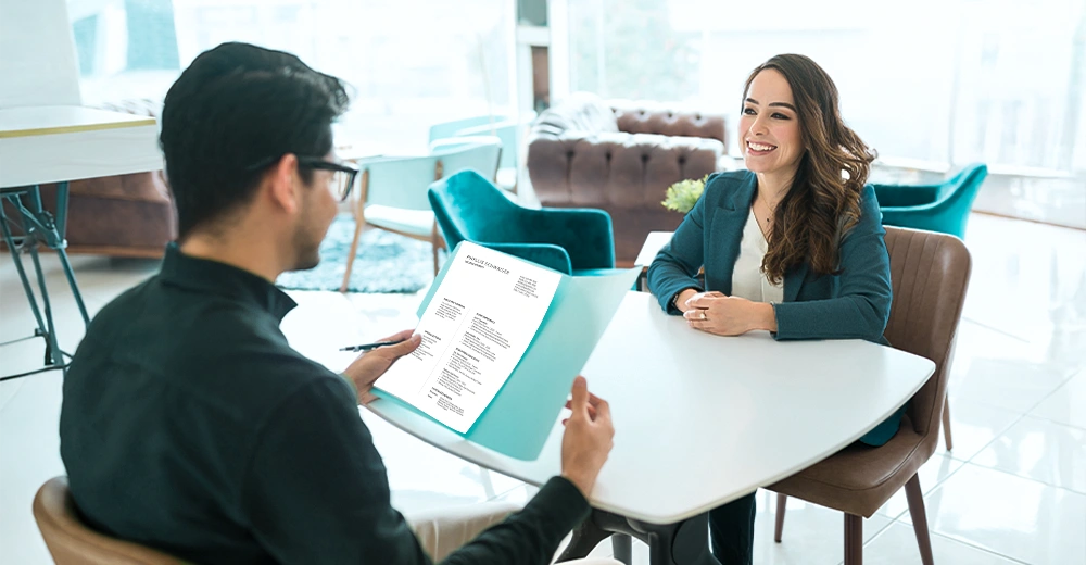 A recent graduate confidently handing a resume to a hiring manager during a job interview.