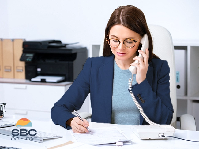 An administrative assistant attending a customer call at work, showcasing customer service orientation.
