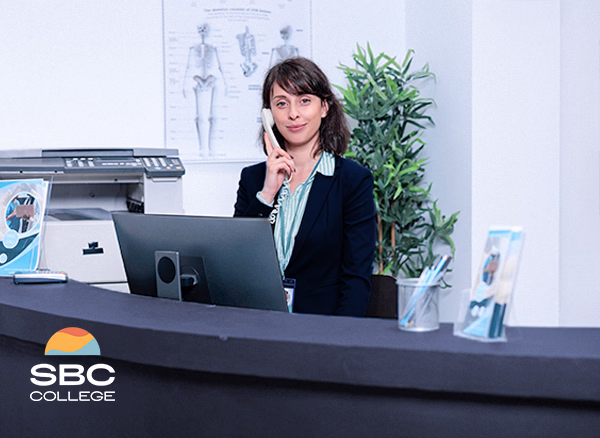 A medical office assistant answering a phone call at a private clinic reception desk.