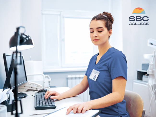 Female medical office administrator updating records on her system in a medical office setting.