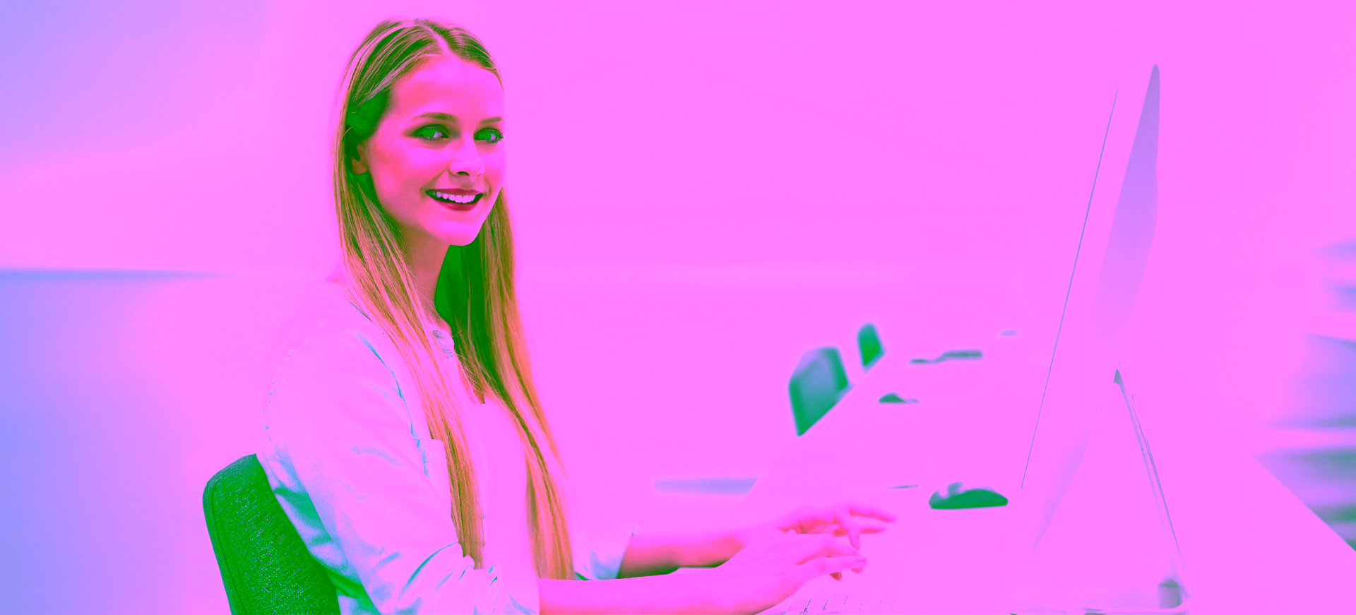 A smiling young woman looks up from her computer.