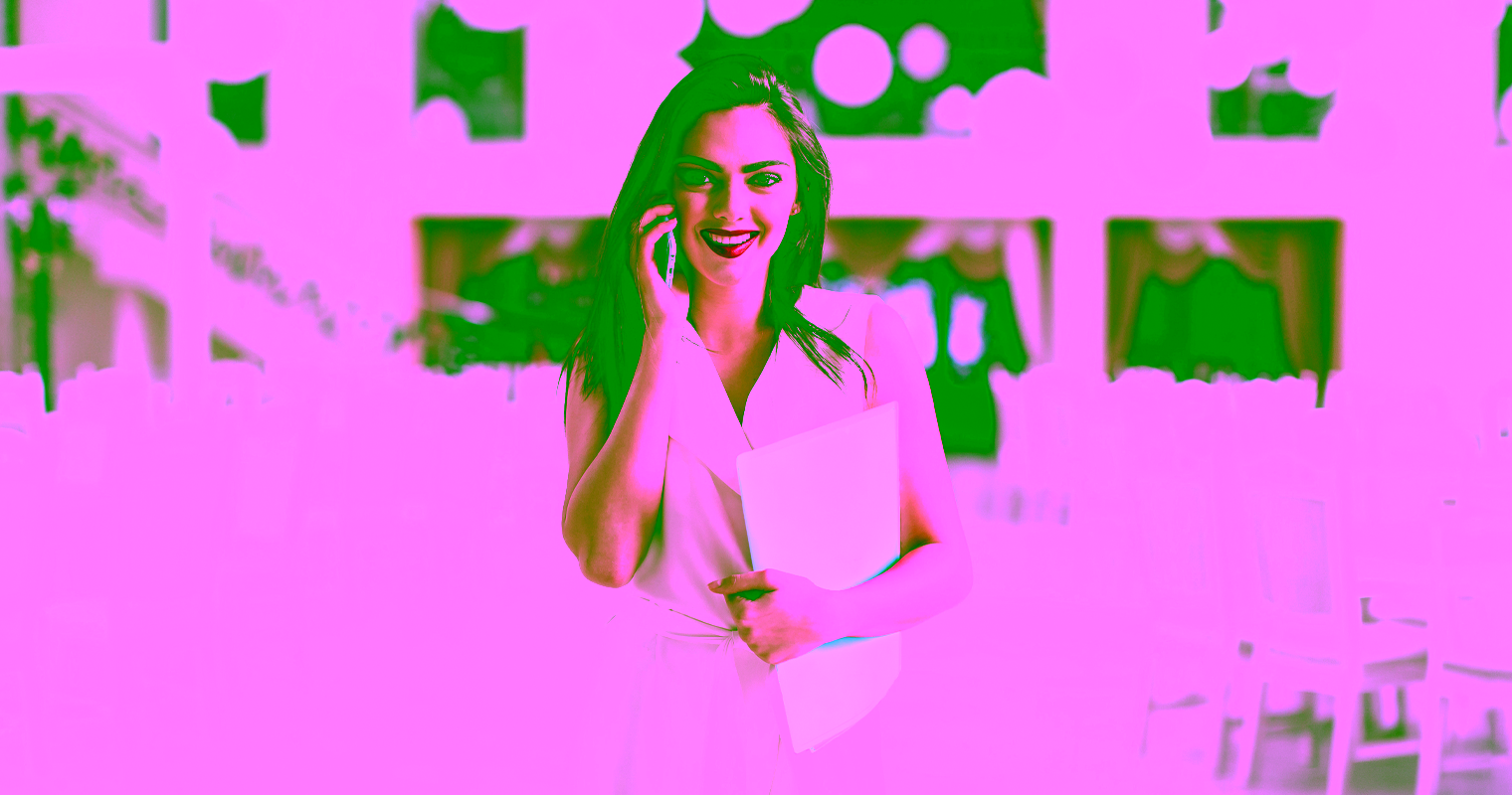 A female event manager speaking on the phone at an event venue while holding a folder.