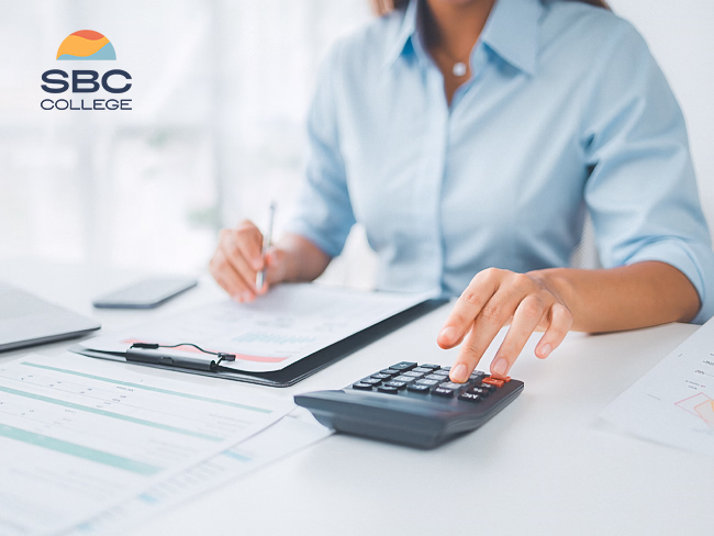 A calculator, balance sheet, and clipboard sit on a desk in front of an accounting and payroll administrator.